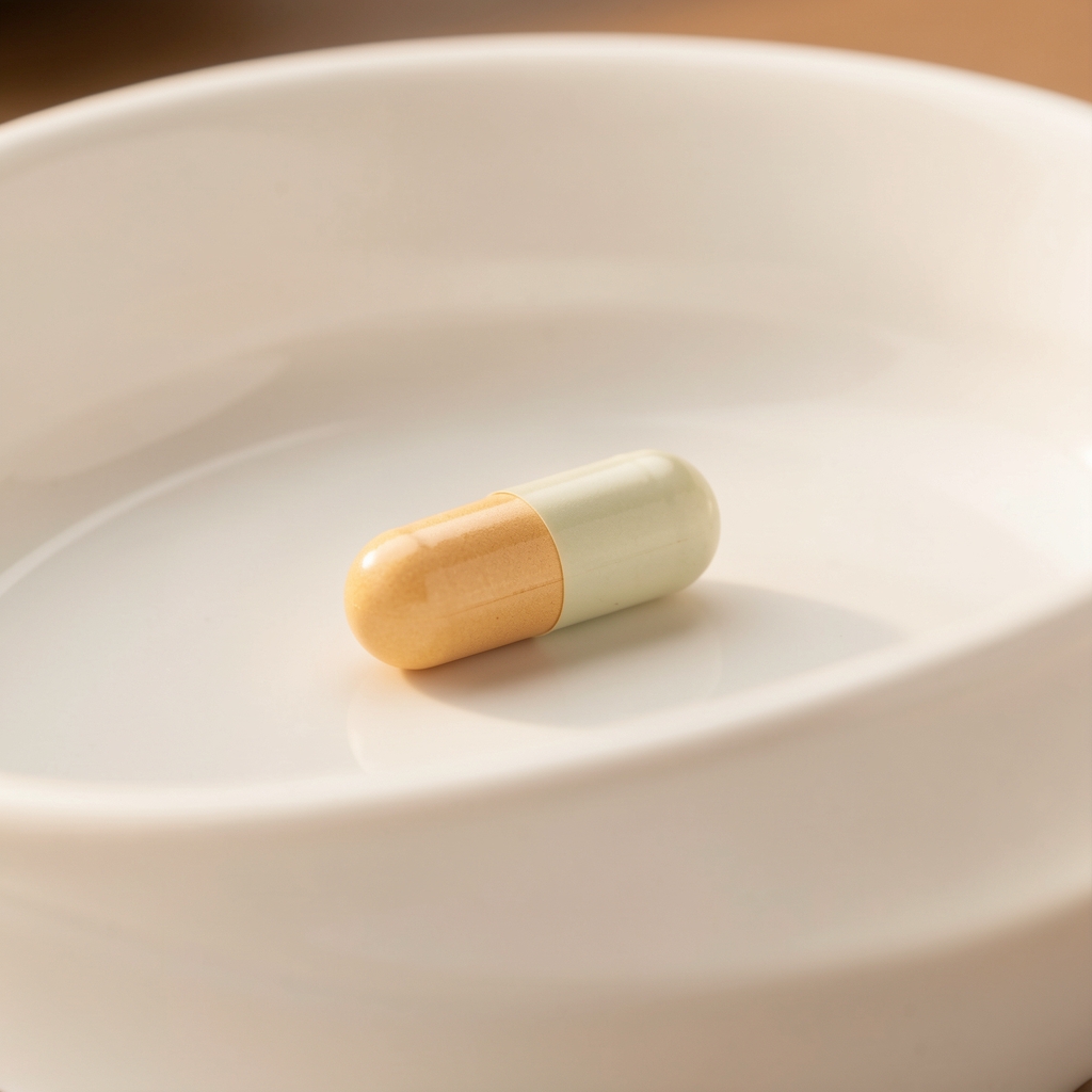 Vitality formula supplement capsule on a clean white ceramic surface with soft warm studio lighting, composition reference